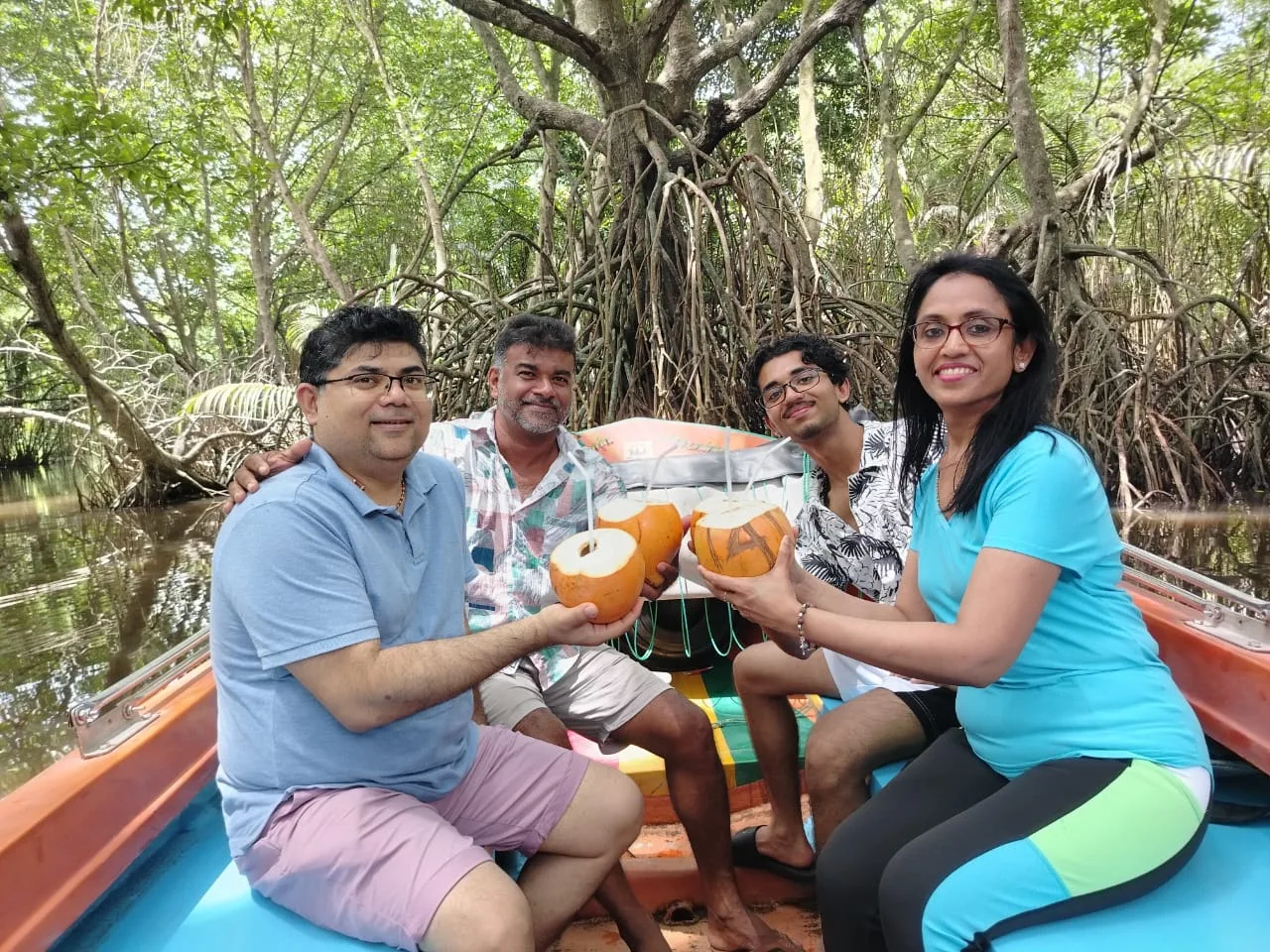 Four guests raising fresh king coconuts together aboard a boat among the Bentota mangroves