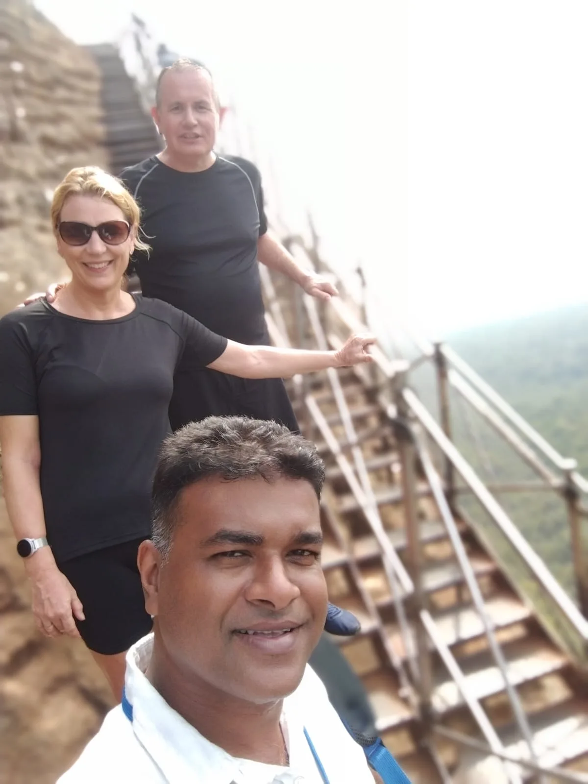 A Sammy Tours guide taking a selfie with two guests on the metal stairway at Sigiriya Rock Fortress