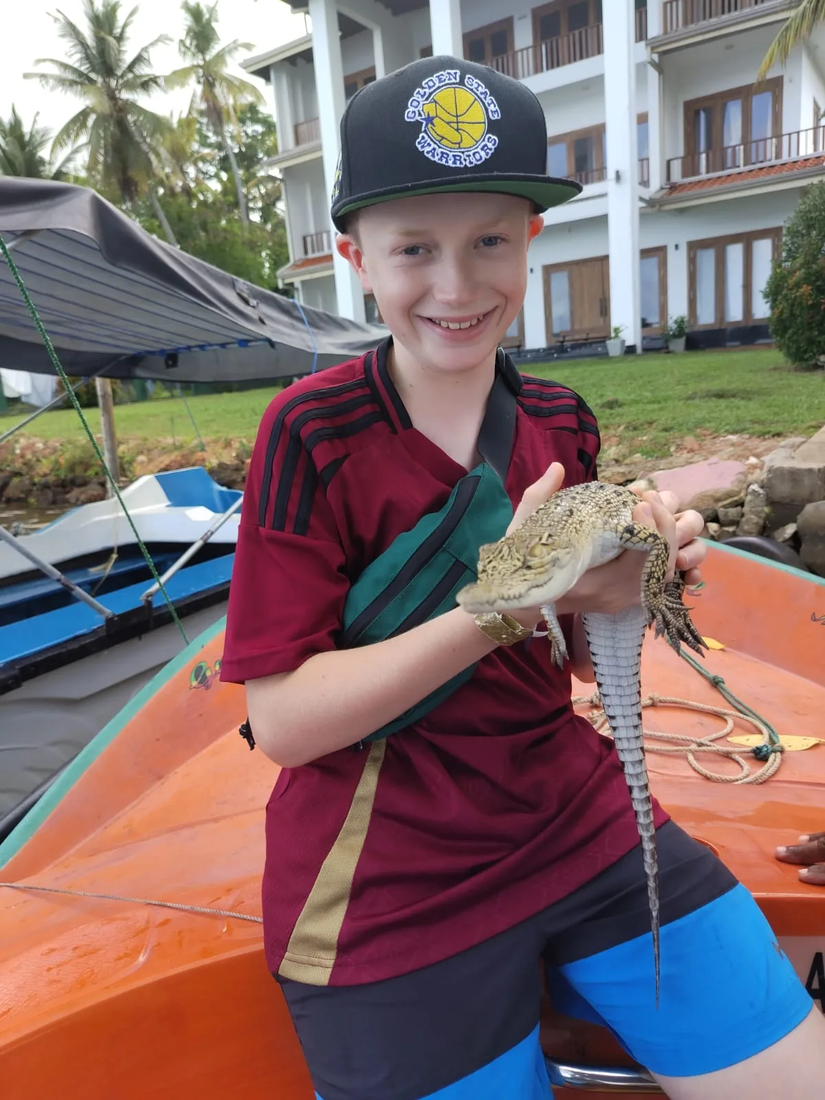 A smiling young guest carefully holding a small crocodile while seated on a Bentota river boat