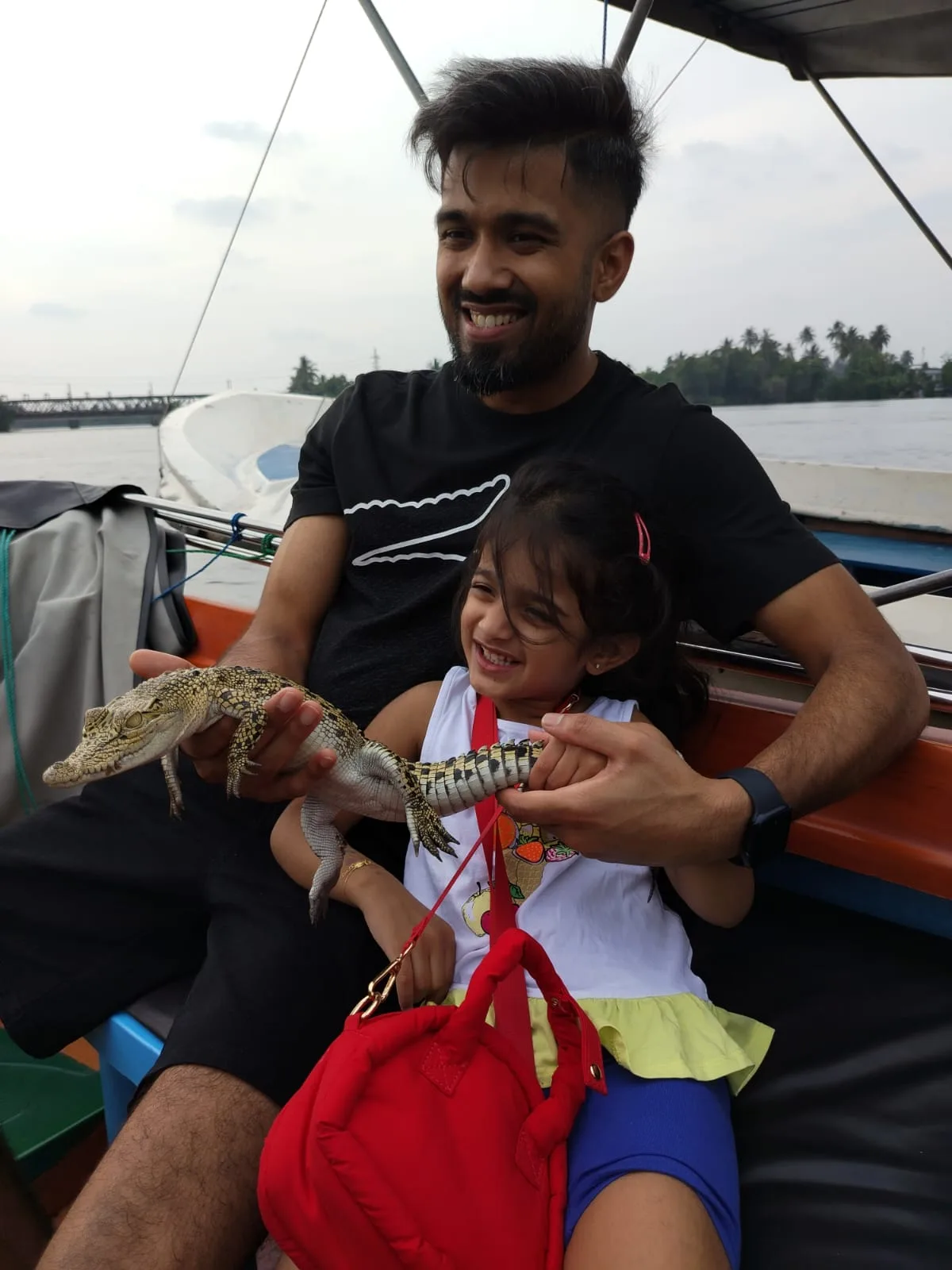 An adult and child carefully holding a young crocodile aboard a Bentota river safari boat